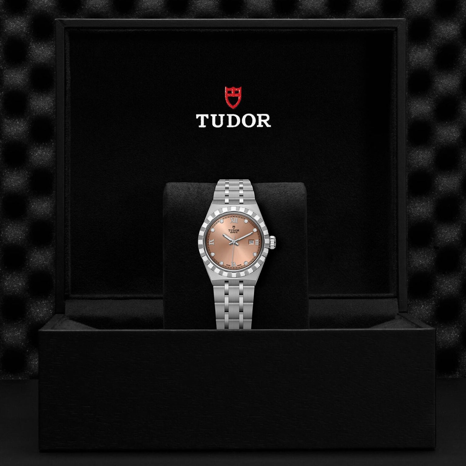 A TUDOR Royal wristwatch is showcased in an open black Tudor-logo box, featuring a salmon dial, automatic movement, and metal bracelet that emphasize its sport chic elegance.