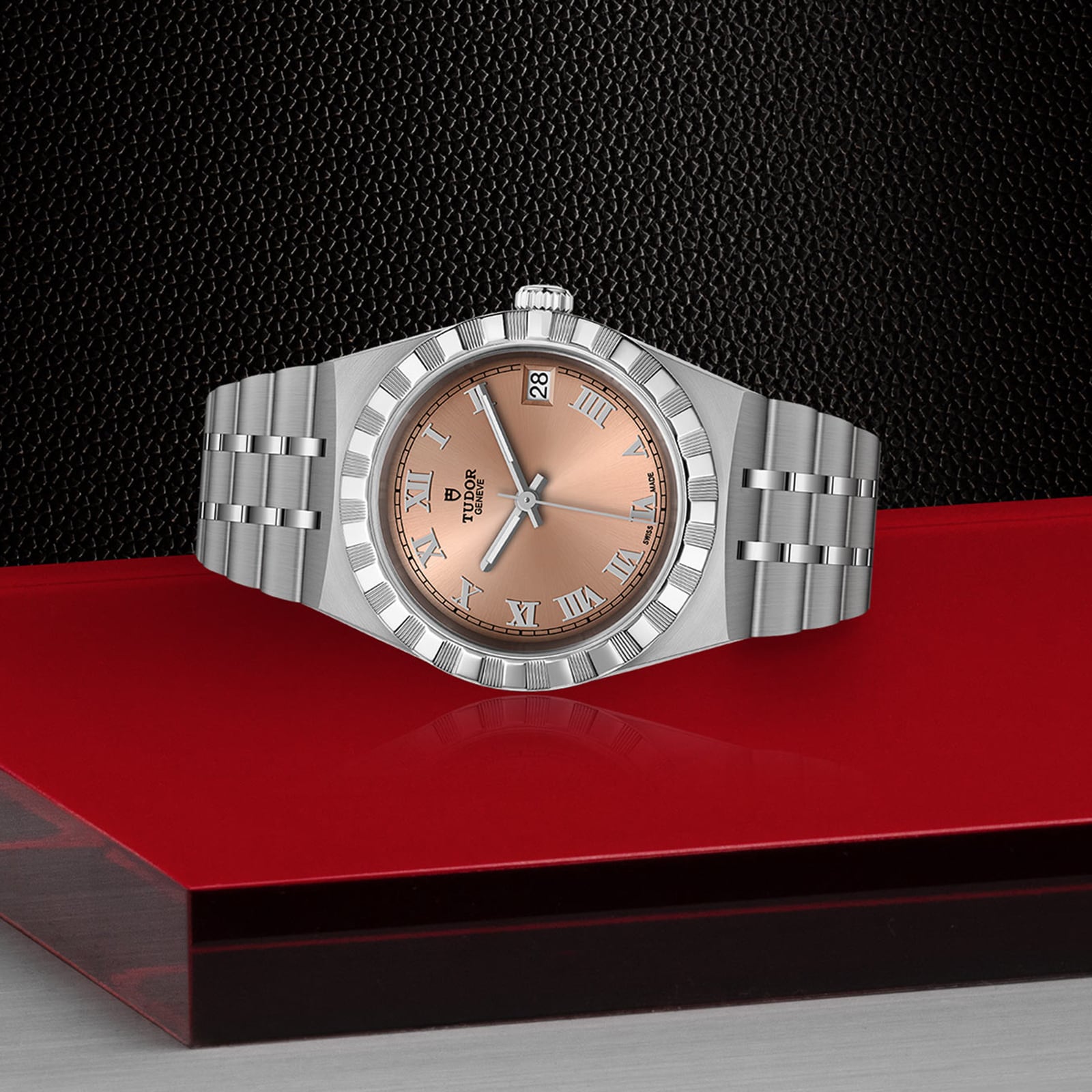 A TUDOR Royal silver wristwatch with a salmon dial and Roman numerals, automatic movement, is presented on a red and black textured surface for a sport chic look.