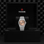 A TUDOR Royal wristwatch with a silver metal band and salmon dial, featuring automatic movement, is displayed upright in a black Tudor-branded presentation box.