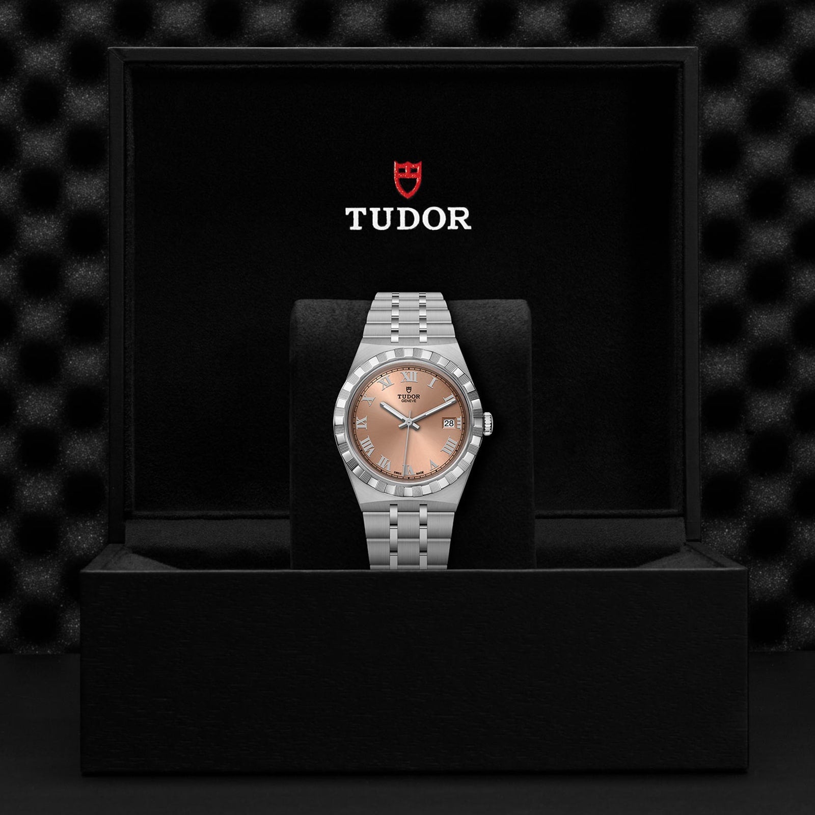 A TUDOR Royal wristwatch with a silver band and salmon dial, featuring automatic movement, is displayed upright in an open black presentation box branded with the TUDOR logo.