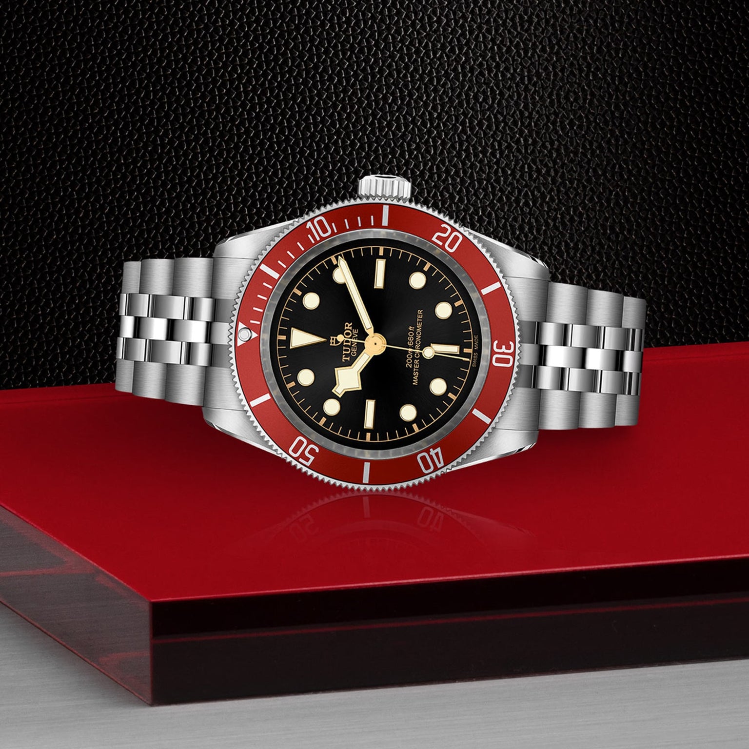 The TUDOR Black Bay wristwatch features a stainless steel case, burgundy bezel, and black dial, showcased on a red and black surface with a textured black backdrop.