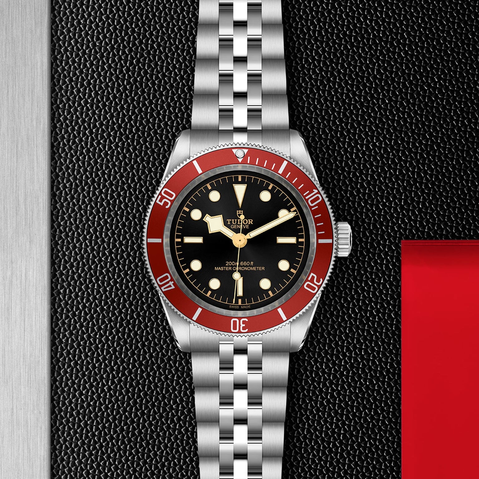 The TUDOR Black Bay stainless steel wristwatch features a burgundy bezel, black dial, and silver bracelet, displayed on a textured black background.