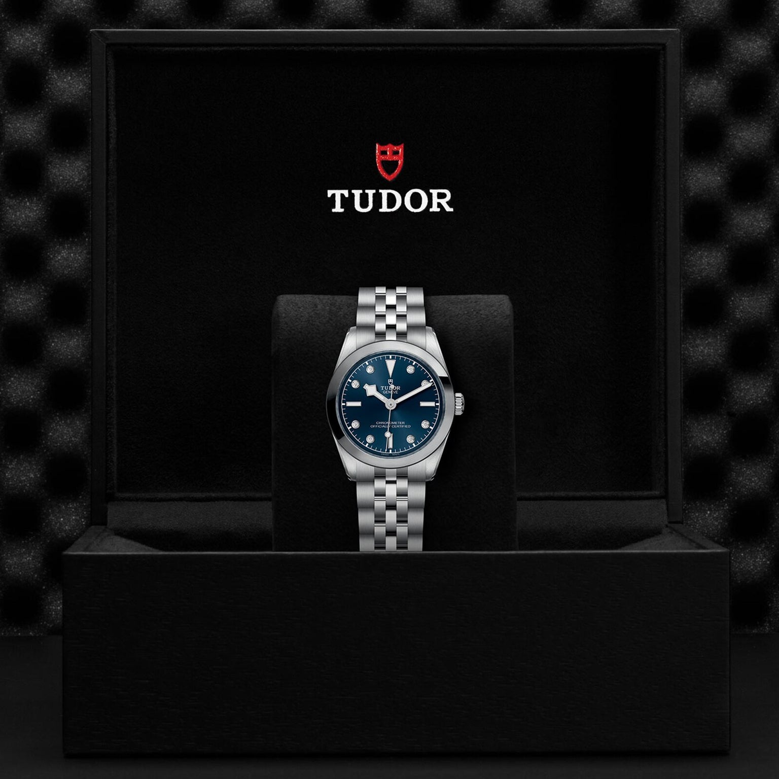 A TUDOR Black Bay One 31 silver wristwatch with a blue dial, displayed in an open black TUDOR watch box.