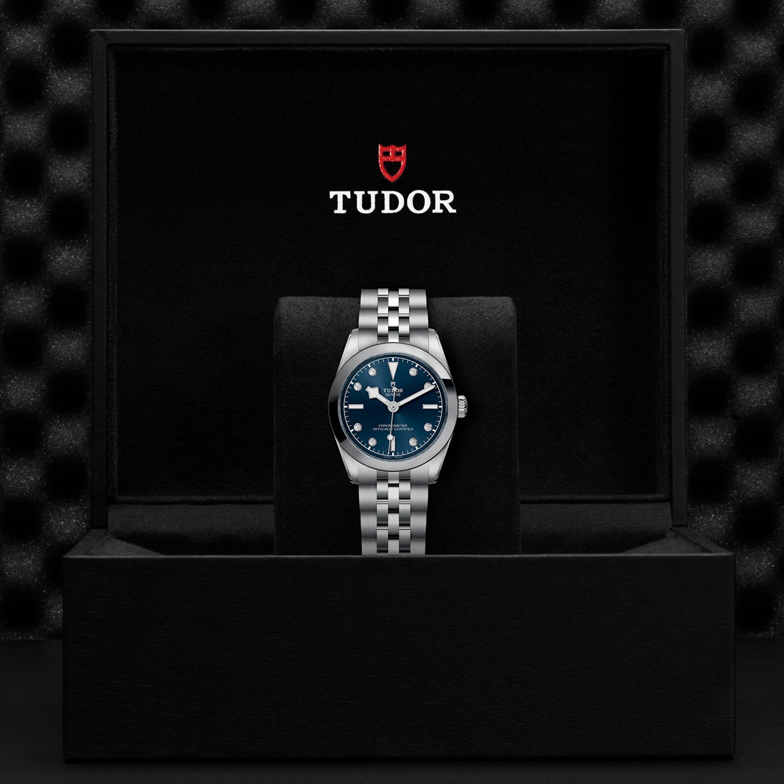 A TUDOR Black Bay One 31 silver wristwatch with a blue dial, displayed in an open black TUDOR watch box.
