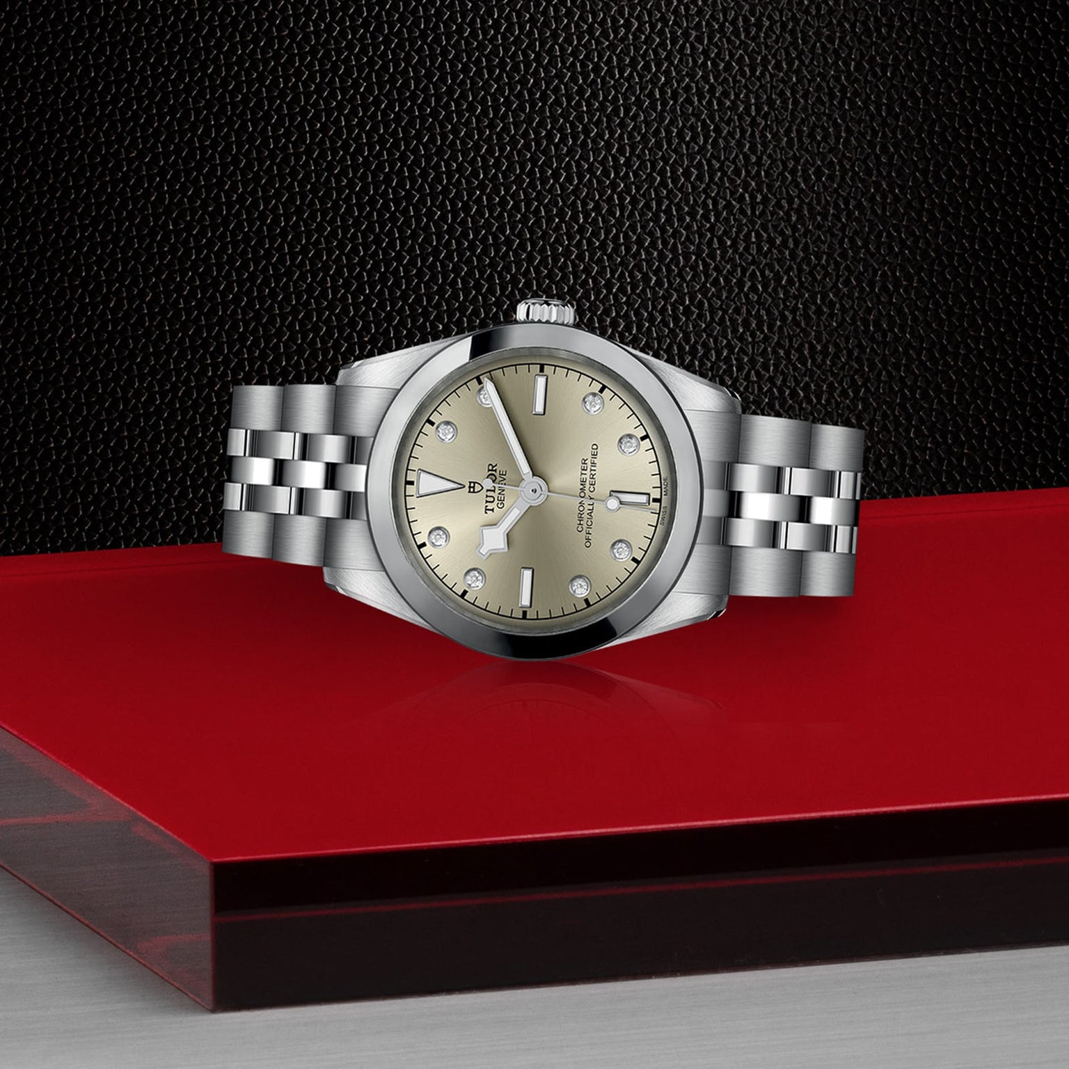 A TUDOR Black Bay One 31 wristwatch with a silver case and champagne dial, displayed on a red and black platform.