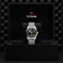 A TUDOR Black Bay One 39 wristwatch with a black dial and metal bracelet is displayed in an open black TUDOR box, highlighting its unisex style and precision Manufacture Calibre.