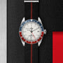 The TUDOR Black Bay GMT wristwatch features a black strap with a red stripe, blue and red bezel, opaline dial, and date display. Shown on a textured black and silver background, it’s ideal for stylishly tracking multiple time zones.