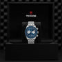 A TUDOR Black Bay Chrono wristwatch with a blue dial and silver bracelet stands upright in an open black presentation box featuring the TUDOR logo, as seen in select Tudor Boutiques.