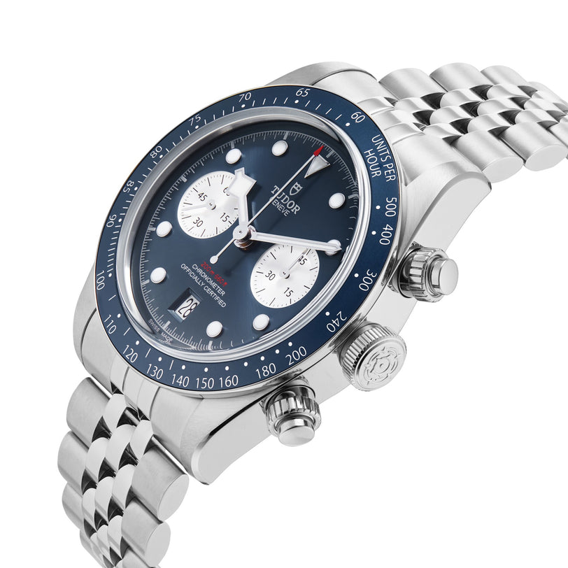 The TUDOR Black Bay Chrono, featuring a silver case, blue bezel, blue dial with two white subdials, and a metal bracelet, is displayed at an angle on a white background. Available exclusively at select TUDOR Boutiques.
