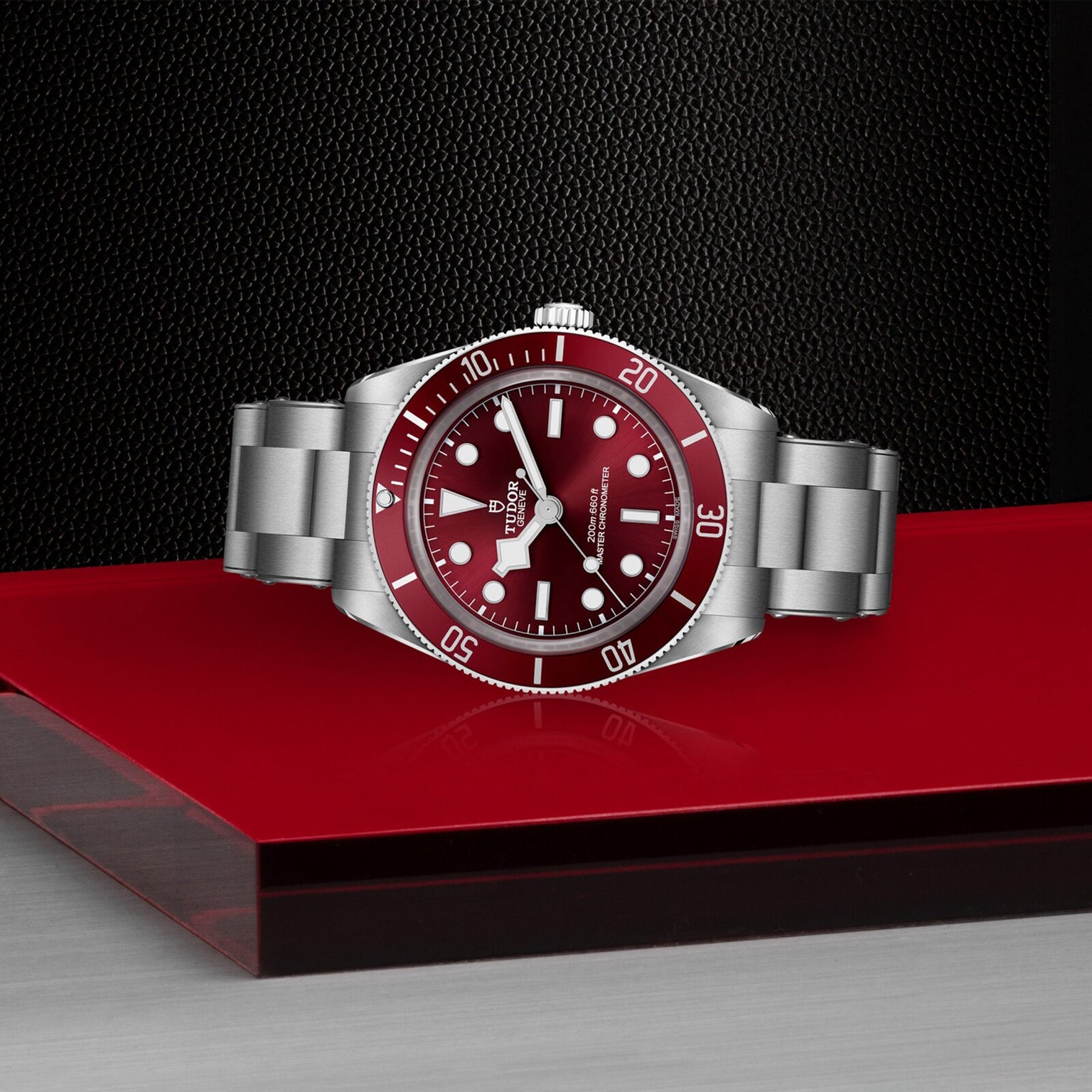 The TUDOR Black Bay 58 wristwatch with a stainless steel case features a red bezel and dial, displayed on a red and silver surface.