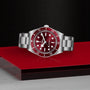 The TUDOR Black Bay 58 wristwatch with a stainless steel case features a red bezel and dial, displayed on a red and silver surface.
