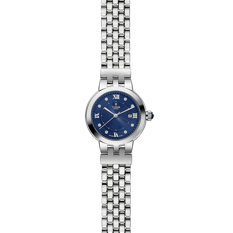 The TUDOR Clair de Rose wristwatch features a blue dial with Roman numerals and a silver metal link band, shown on a white background.