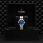 A TUDOR Clair de Rose wristwatch with a blue dial and silver band is displayed in an open black TUDOR box.
