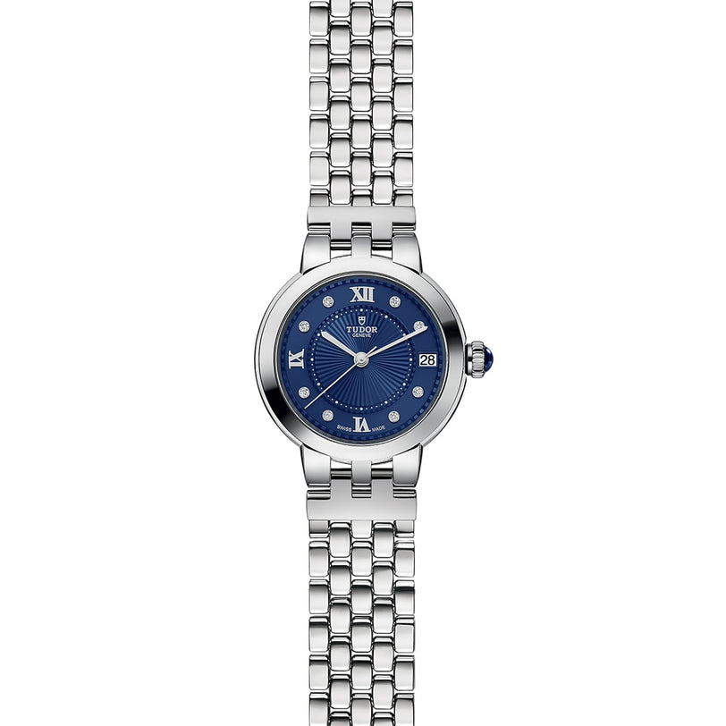The TUDOR Clair de Rose is a silver wristwatch featuring a blue face with Roman numerals and a metal link band.