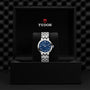 A silver TUDOR Clair de Rose wristwatch with a blue face, presented in a black TUDOR-branded display box.