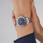 A TUDOR Clair de Rose wristwatch with a silver band and blue face featuring Roman numerals on a persons wrist.