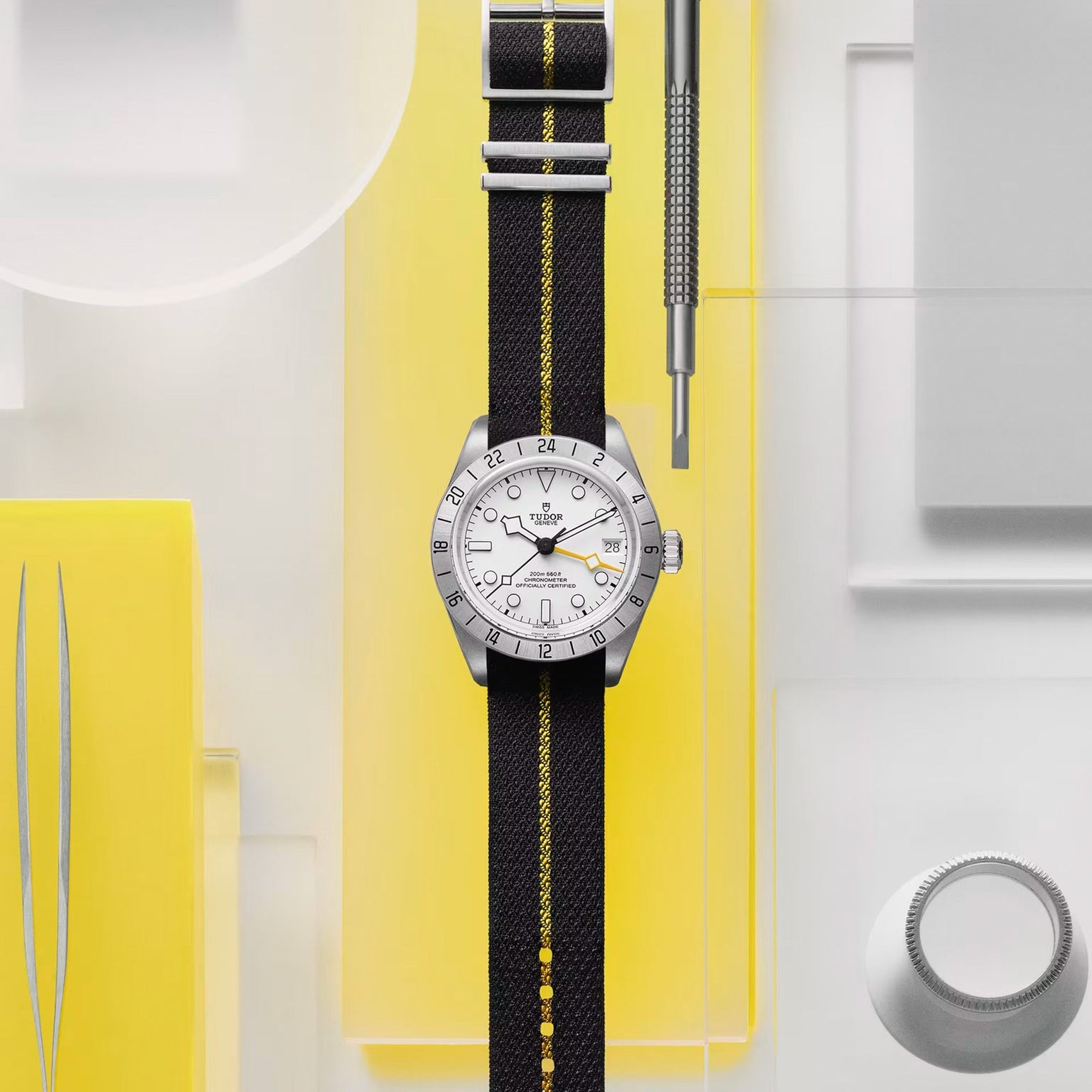 The TUDOR Black Bay Pro wristwatch with a black and yellow strap is displayed on a yellow and white geometric background.