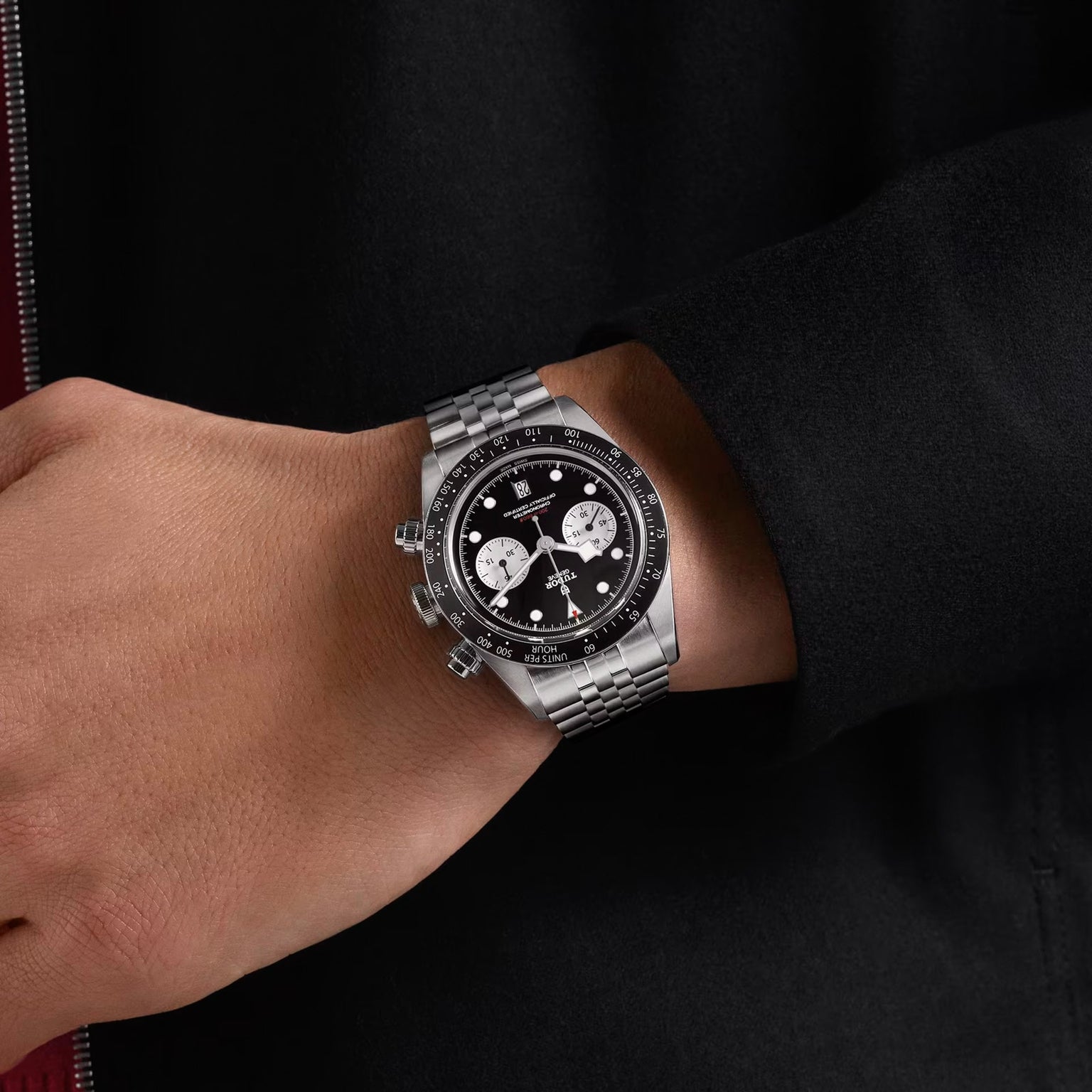 A hand wearing the TUDOR Black Bay Chrono, a silver wristwatch featuring a black dial and three white subdials.