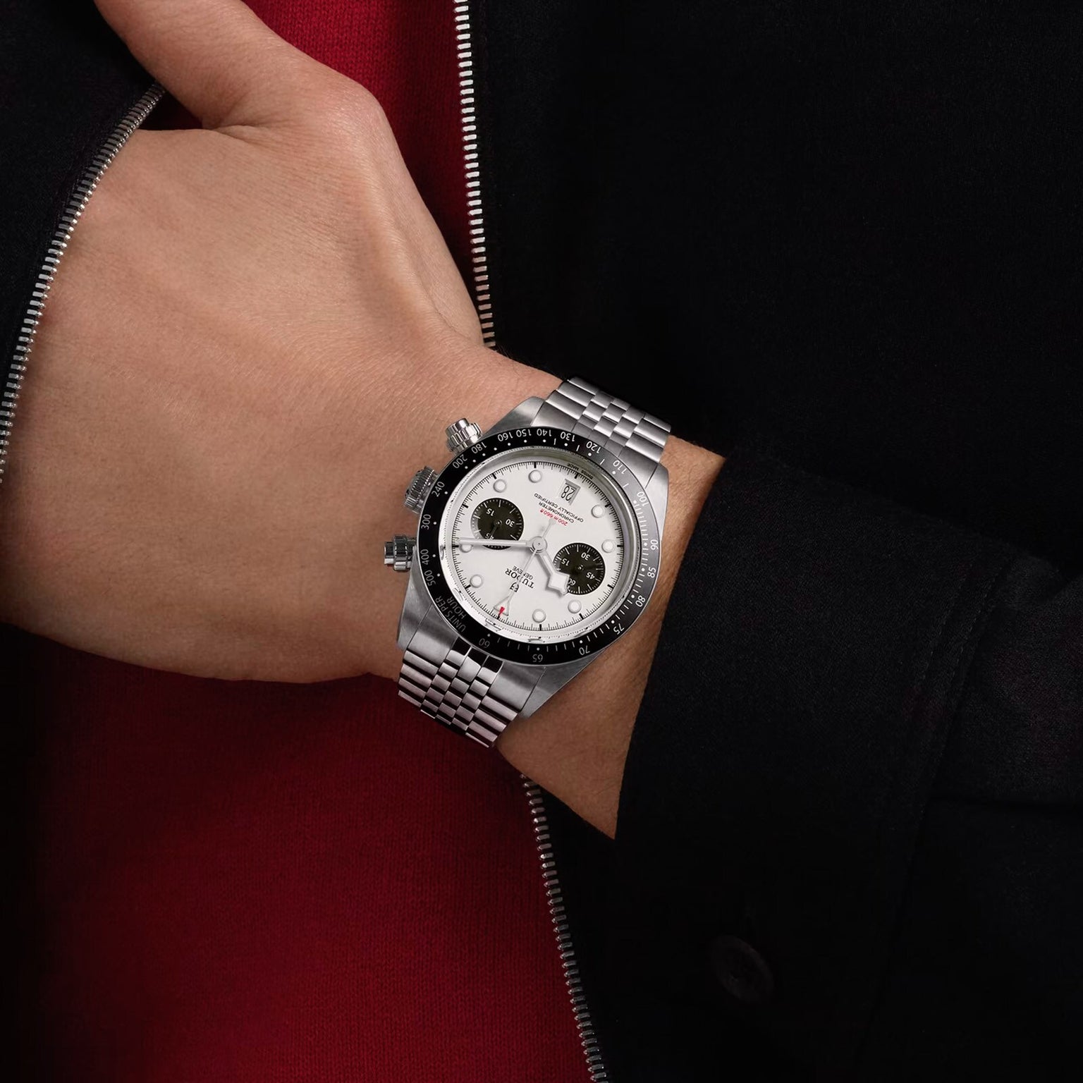 A person wearing a TUDOR Black Bay Chrono, a silver chronograph watch with a white dial and black subdials, on their left wrist.