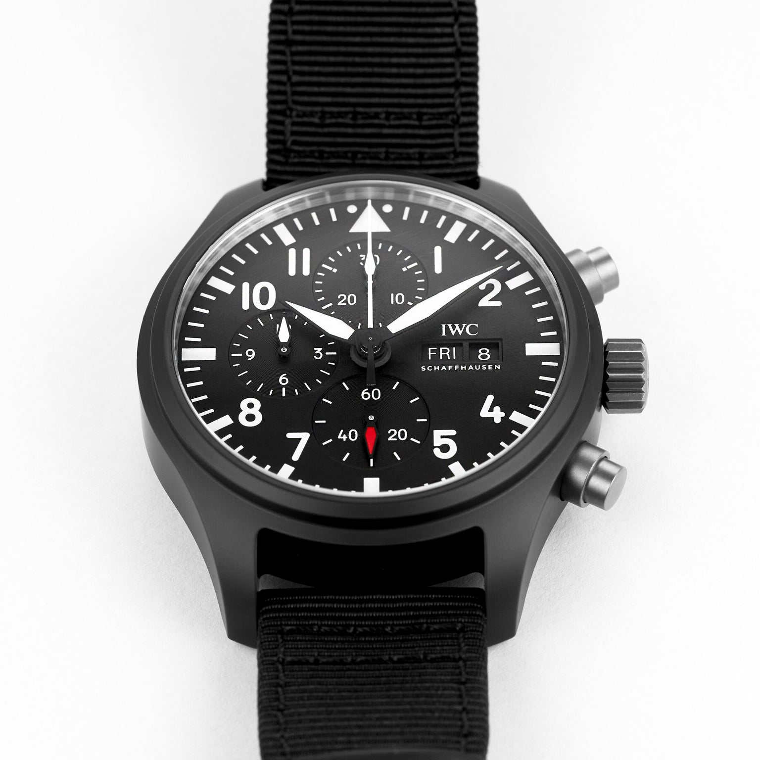 The IWC Schaffhausen Pilots Watch Chronograph Top Gun features a black case, black nylon strap, and displays time, day, and date on a white dial.