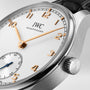 Close-up of the IWC Schaffhausen Portugieser Automatic 40 wristwatch with gold hour markers and hands, white dial, small seconds subdial, black leather strap, and IWC’s 82200 calibre featuring a Pellaton winding system.