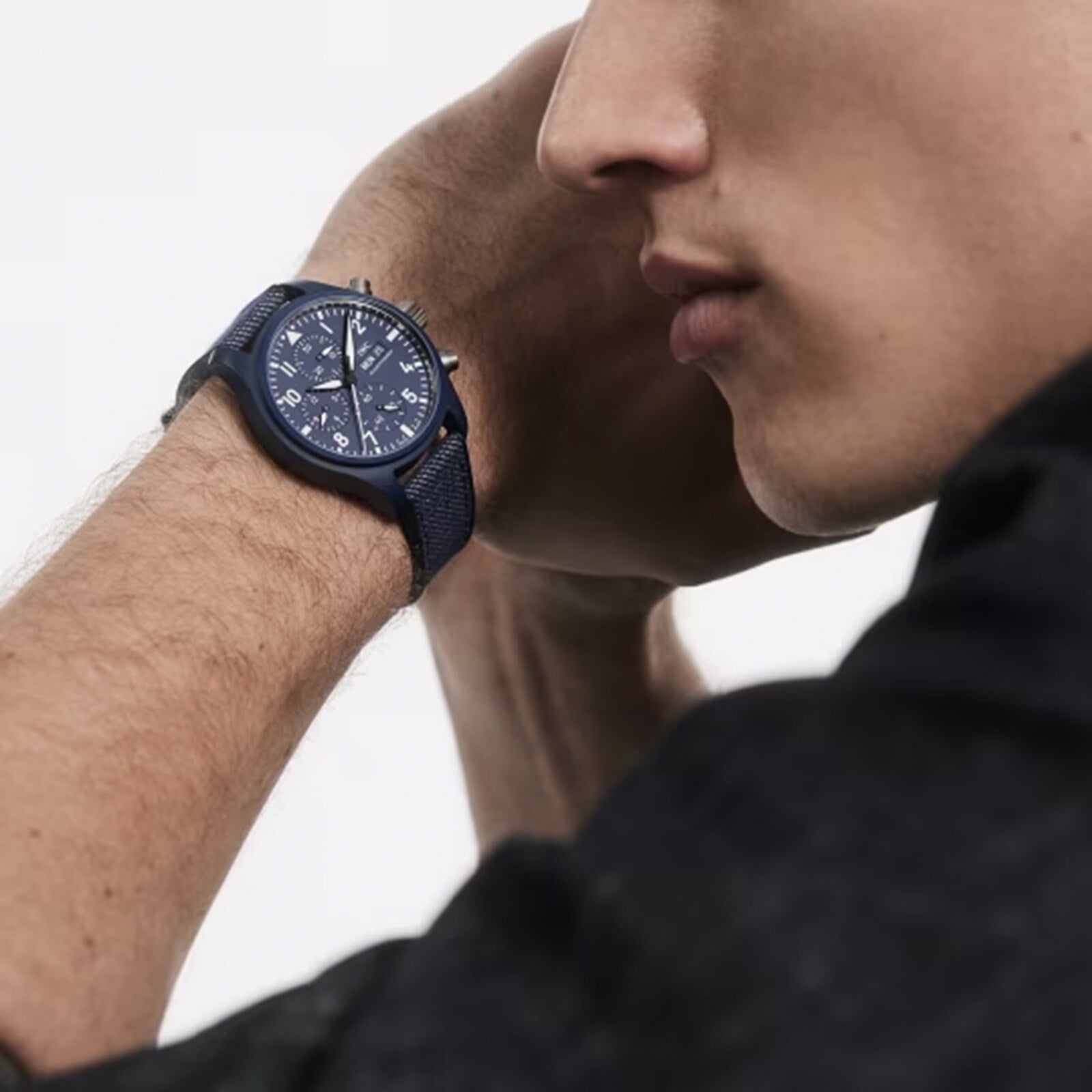 A person wearing an IWC Schaffhausen Pilots Watch Chronograph 41 Top Gun Oceana with a round face and multiple dials holds their hand near their face, partially visible against a plain background.