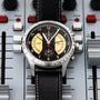 The Reservoir Sonomaster Chronograph Vintage wristwatch with a black leather strap rests on an audio mixing console with sliders and knobs.