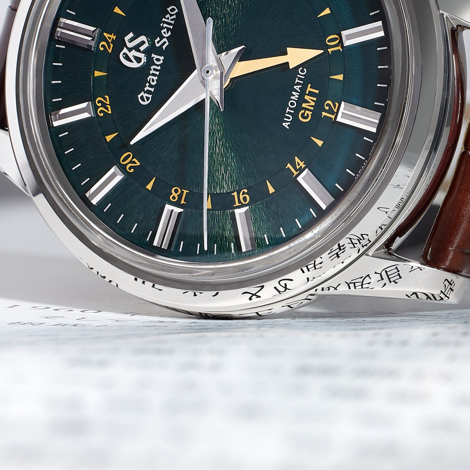 Close-up of the Grand Seiko Automatic GMT Elegance wristwatch with a Mount Iwate dial in British Racing Green and a brown leather strap, displayed on paper featuring Japanese text.