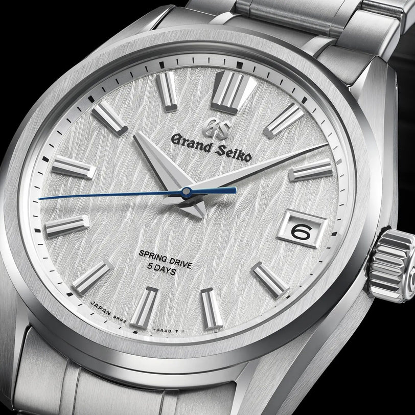Close-up of the Grand Seiko Spring Drive 5 Days Evolution 9, featuring a textured silver dial inspired by Japanese nature, silver hour markers, blue second hand, date at 3 o’clock, and Spring Drive 5 Days above 6 o’clock.