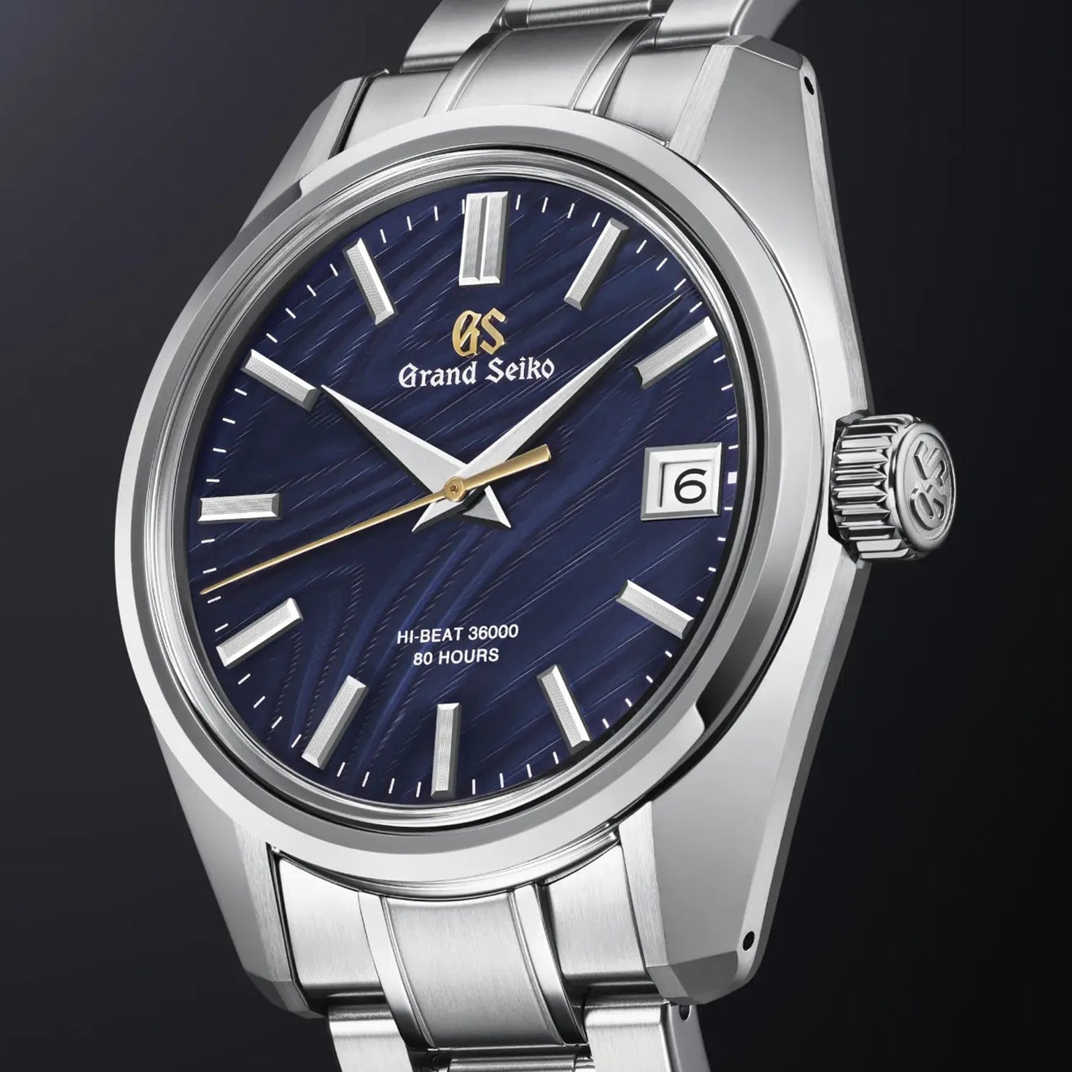 The Grand Seiko Hi-Beat Heritage wristwatch, handmade in Japan, features a blue patterned dial, silver hour markers, date window at 3 o’clock, and a stainless steel case and bracelet—precision in every detail.