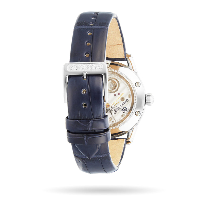 The Grand Seiko Manual Elegance is a luxury mechanical watch with a blue leather strap and visible Caliber 9S64 movement on the back, shown against a white background.