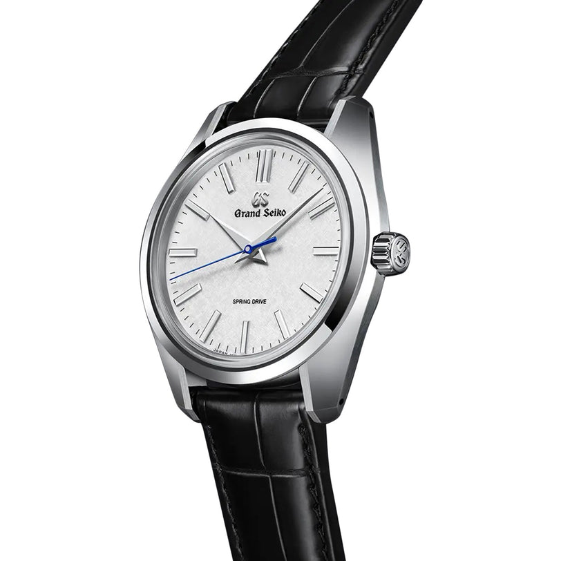 The Grand Seiko Spring Drive Heritage features a silver dial, blue second hand, black leather strap, and stainless steel case with Spring Drive technology, elegantly displayed at an angle.