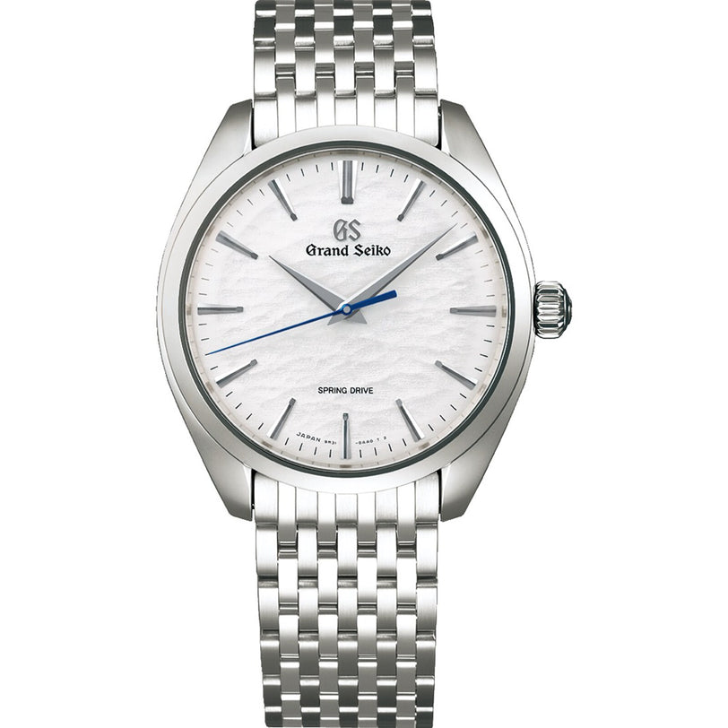 The Grand Seiko Spring Drive Manual Elegance features a textured white dial, blue second hand, and metal bracelet, inspired by Lake Suwa, displaying the time as 7:08:38.