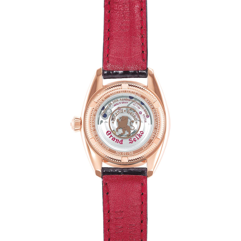 A close-up of the Manual Elegance by Grand Seiko showcases its mechanical movement through a transparent caseback, highlighted by a red strap and gold casing.