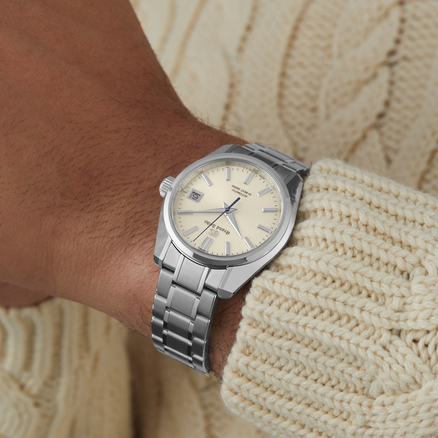 A Grand Seiko Hi-Beat Heritage wristwatch with a cream dial and date display, elegantly worn on the wrist, pairs perfectly with a cream cable-knit sweater.