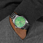 Someone with their hand in the pocket of gray textured pants wears a Grand Seiko Hi-Beat Limited Edition Heritage, a silver wristwatch featuring a green dial and date window.