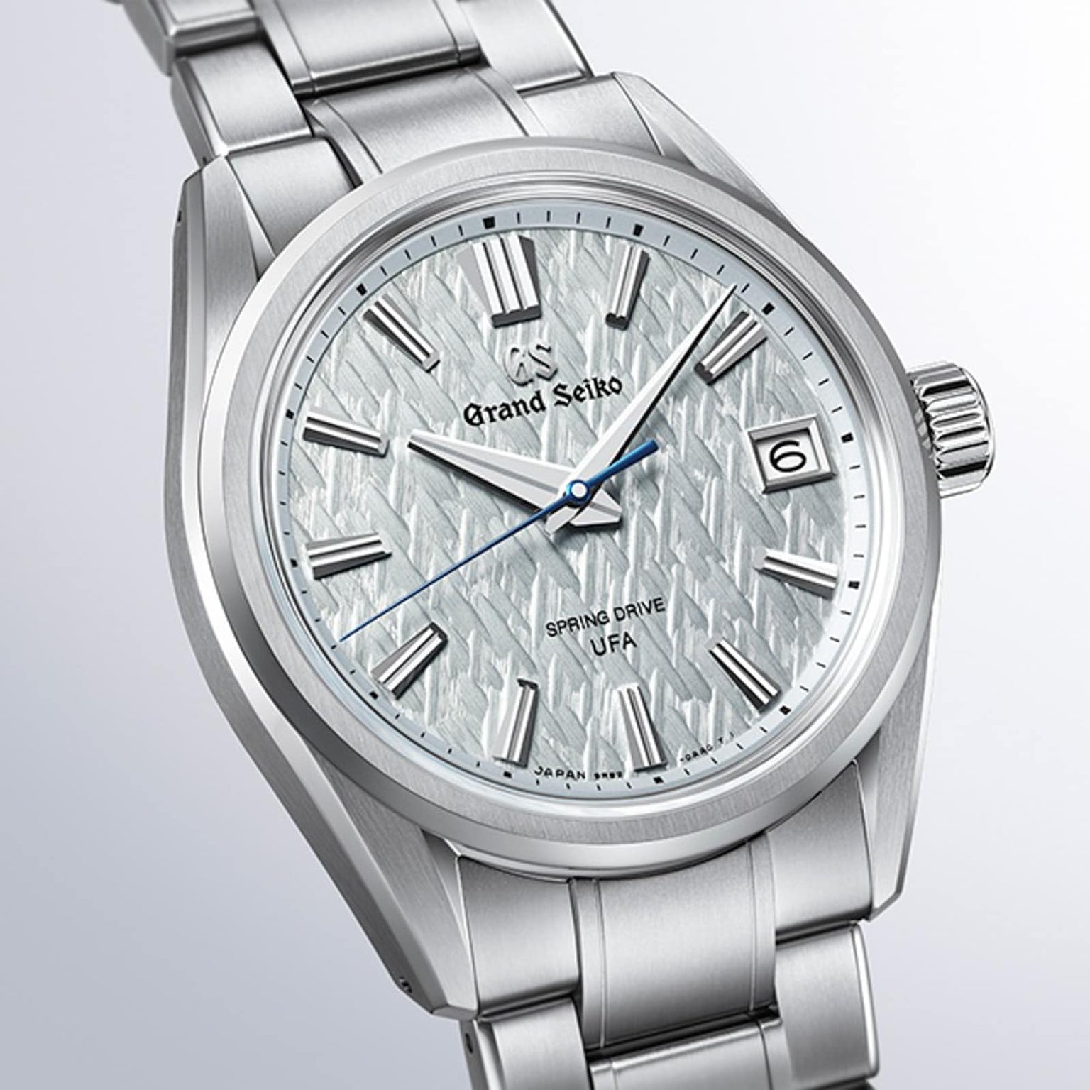 The Grand Seiko Spring Drive U.F.A Evolution 9 wristwatch features a silver case, textured white dial, date window, and blue second hand.