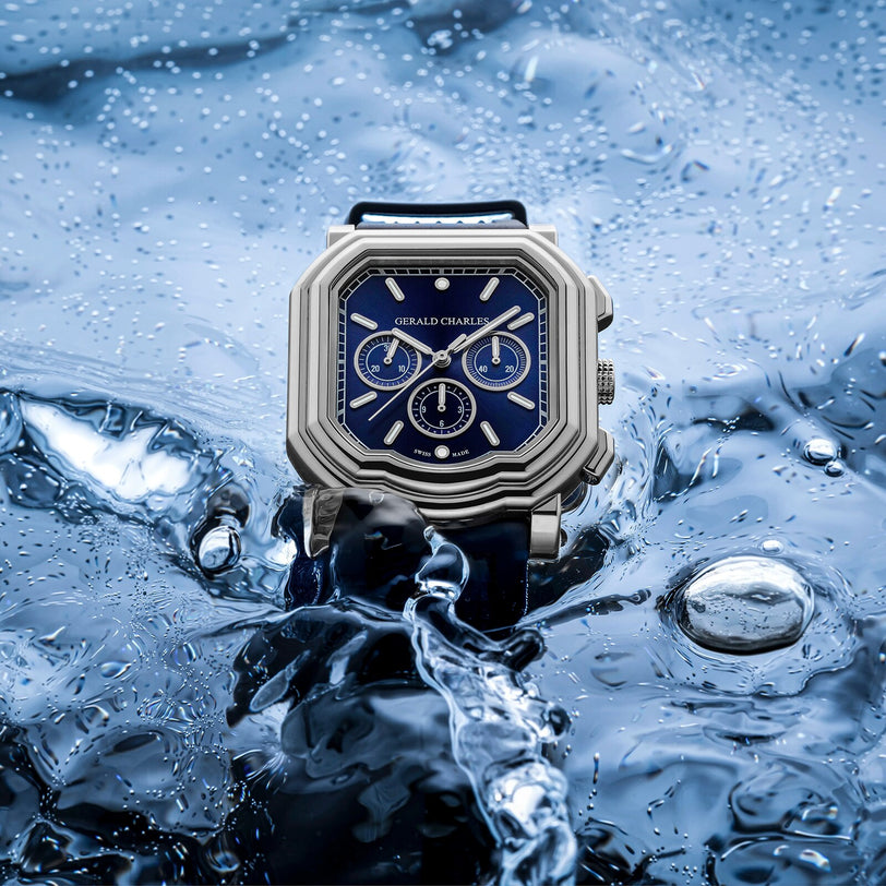The Gerald Charles Maestro 3.0 Chronograph, featuring a blue dial and silver case, is partially submerged in water as splashes accentuate its precise craftsmanship.