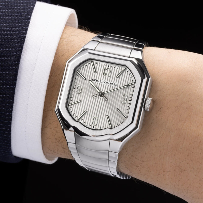 The Masterlink Silver by Gerald Charles, a luxury silver watch with a geometric face, is worn on the wrist with a dark suit and white shirt.