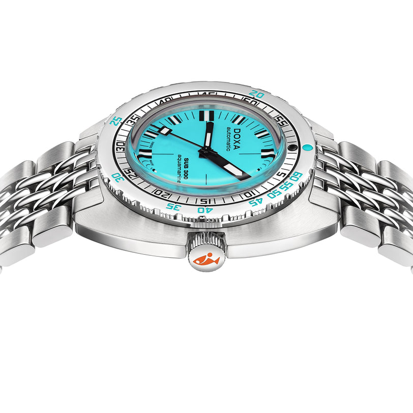 The DOXA Sub 300 Aquamarine is a stainless steel diver’s watch with a turquoise dial, black markers, and metal bracelet, shown from a side angle. The crown displays an orange fish logo.
