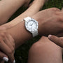 A person wearing a DOXA Sub 200 Whitepearl watch with a white strap sits on grass outdoors, while another persons legs appear in the background.
