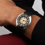 A person in a black long-sleeve shirt showcases the DOXA Army Bronze by DOXA, featuring a black strap, beige dial, orange second hand, and Super-LumiNova® for enhanced visibility.