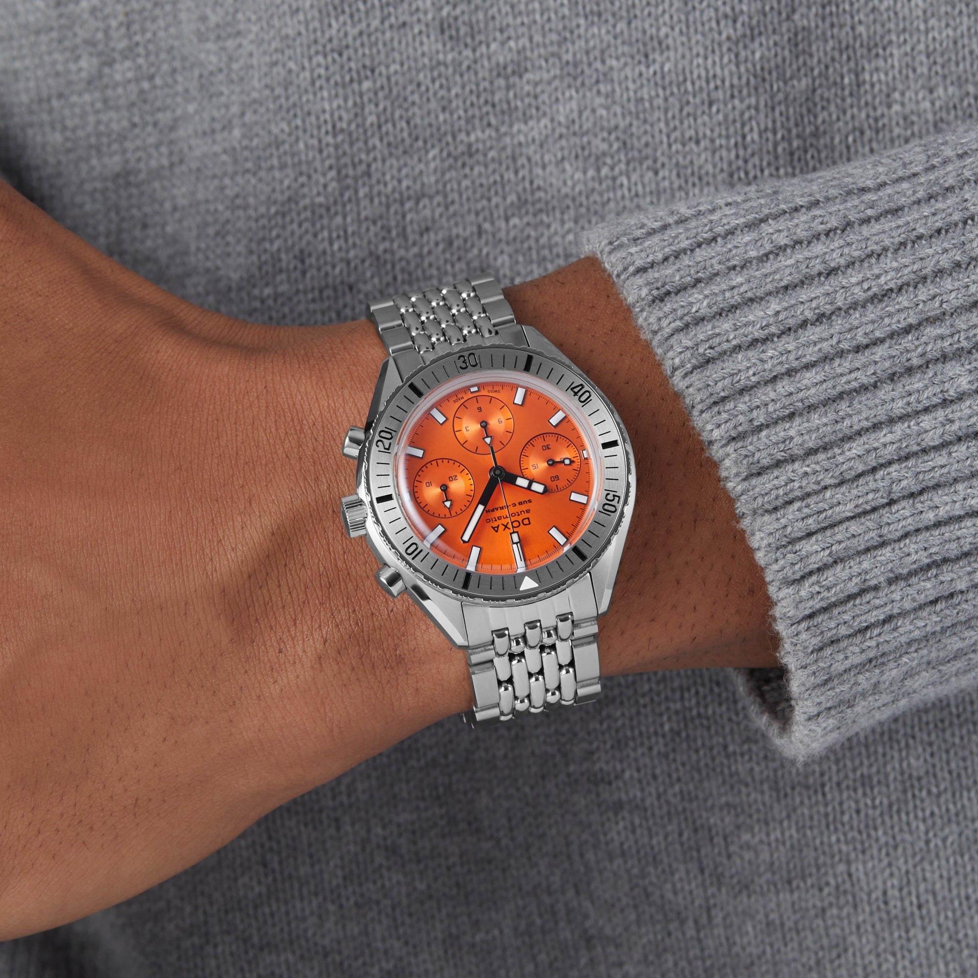 A person wearing the DOXA Sub 200 C-Graph II Professional stainless steel dive watch with an orange dial and multiple subdials, dressed in a light gray ribbed sweater.