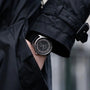 A person in a black coat wears the Louis Erard Petite Seconde Guilloché Anthracite Black wristwatch, hand partially in their coat pocket.