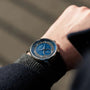 A person wearing the Louis Erard Petite Seconde Guilloché Anthracite Blue wristwatch, featuring a blue face with silver details, is seen outdoors in natural light.