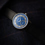 The Louis Erard Petite Seconde Guilloché Anthracite Blue wristwatch, featuring a blue dial and black strap, is displayed on a dark fabric background.