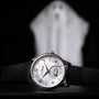 The Louis Erard La Petite Seconde Louis Horror x seconde/seconde/ wristwatch with a black strap is in focus, set against a dark background featuring a blurry ghostly figure.