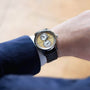 A person in a blue suit wears the Louis Erard Le Régulateur Louis Erard x Massena LAB Gold wristwatch, featuring a gold dial and two subdials.