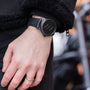 A person wearing the Le Régulateur Louis Erard x Olivier Mosset black watch by Louis Erard and a silver ring on their left hand, dressed in dark clothing.