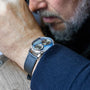 Close-up of a mans wrist wearing the Louis Erard Le Régulateur x Cédric Johner Blue dual-dial watch, with his face slightly blurred in the background.